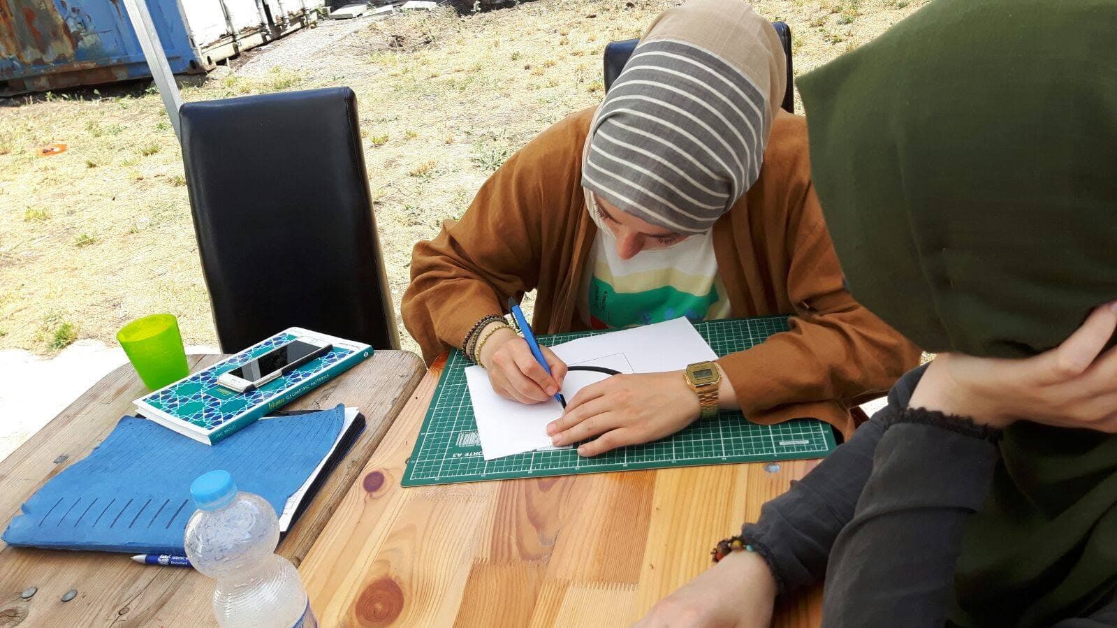 Participantes desenham padrões geométricos em uma mesa ao ar livre na Alemanha