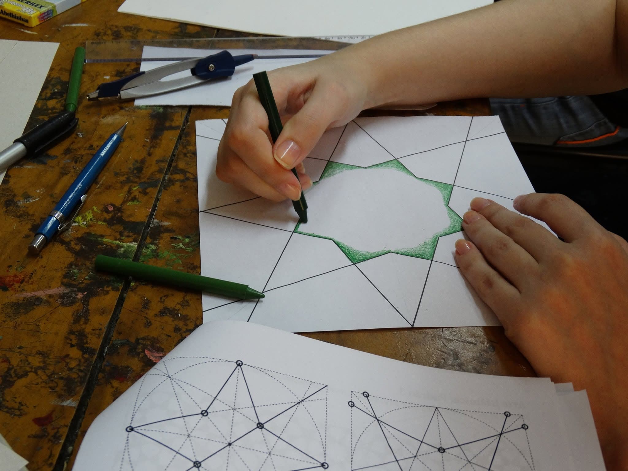 Mãos desenham e colorem um padrão geométrico durante oficina